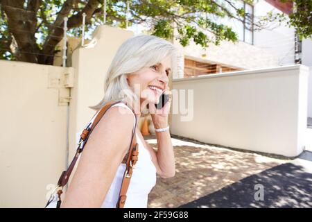 Porträt einer älteren Frau, die mit dem Mobiltelefon geht und spricht Auf dem Bürgersteig Stockfoto