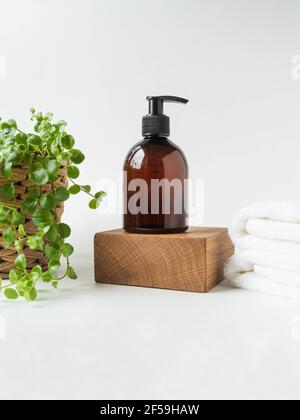 Braune Flasche Mockup für Badeprodukte auf Holz Podium, Spa-Shampoo, Duschgel, Flüssigseife und gestapelte weiße Spa-Handtücher auf weißem Hintergrund. Vorne Stockfoto