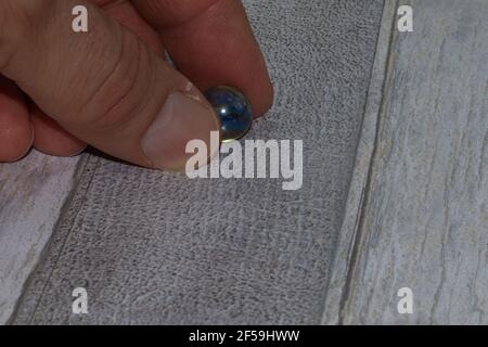 Glassmarmor mit Fingern auf Holzhintergrund gehalten Stockfoto