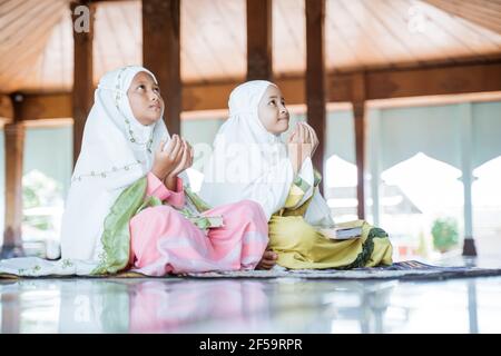 Zwei asiatische muslimische Mädchen sitzen zusammen auf dem Boden Anbetung Und betet für Allah Stockfoto