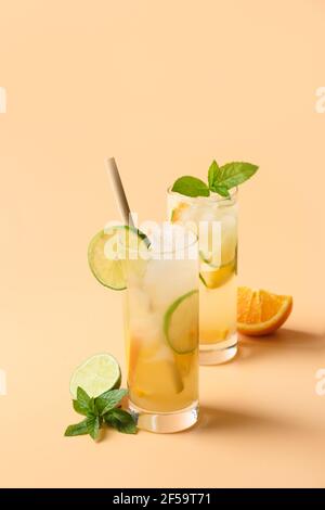 Kalte und erfrischende Limonade oder Cocktail mit Orange- und Limettenscheibe auf beigefarbenem vertikalen Hintergrund. Sommergetränk. Stockfoto