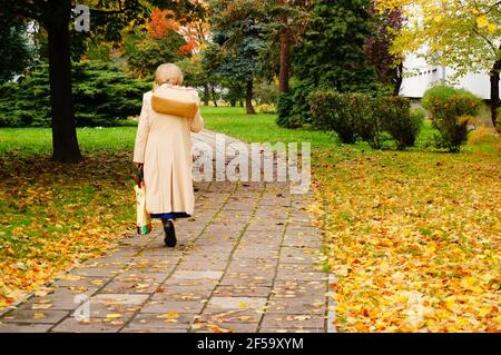 POZNAN, POLEN - 16. Oktober 2013: Ältere Frau, die mit ihrer Einkaufstasche in einem Park spazieren geht Stockfoto