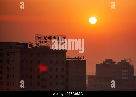 Yunnan, China - 30. MÄRZ 2012: Wohngebäude und Werbetafeln Werbeschilder in chinesischer Sprache auf dem Dach bei Sonnenuntergang. Yunnan. Stockfoto