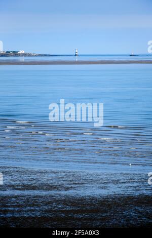 Ein Blick auf einen entfernten Trwyn Du Leuchtturm auf Anglesey über den Lavan Sands bei Ebbe, Llanfairfechan Stockfoto