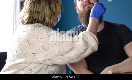 Frau tut Nasenabstrich mit Selbsttest-Kit zu Hause von einem jungen Mann für die Prüfung mögliche Coronavirus-Infektion. Covid-19, Coronavirus, Healht, Selbsttest Stockfoto