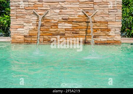 Luxus-Swimmingpool mit einem kleinen Wasserfallbrunnen. Moderne Brunnendetails. Wasserfall-Tropfendesign mit dekorativem beigefarbenem Wandstein. Hochwertige Pho Stockfoto