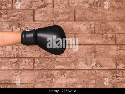 Die Hand eines Mannes in einem schwarzen Ringhandschuh auf dem Hintergrund einer braunen Ziegelwand. Boxkonzept. Stockfoto