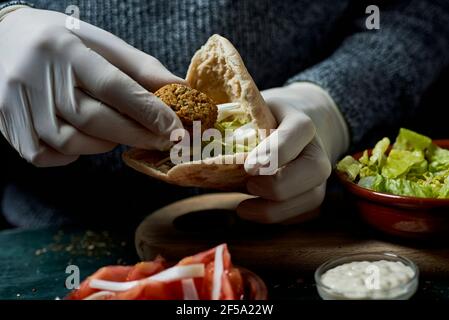 Nahaufnahme eines jungen Mannes, der Latexhandschuhe trägt und ein Falafel-Sandwich in einem Pita-Brot vorbereitet Stockfoto