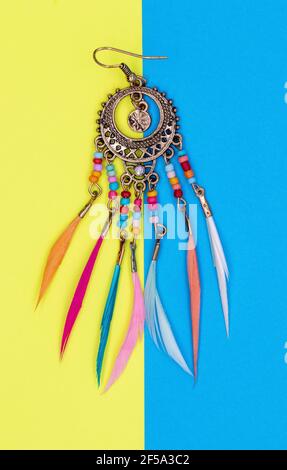 Ethnische Dekorationen auf farbigen Papierblättern.Damenschmuck mit einem runden Metallsockel, mit Perlen und bunten Federn Ohrringe Ringe Amulette Stockfoto
