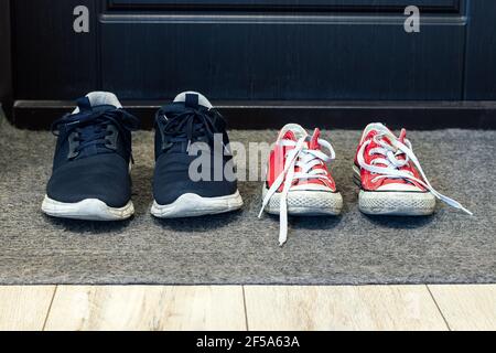 Blaue Familienschuhe und rote Sneakers auf dem Teppich Die Vordertür Stockfoto