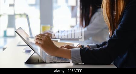 Junge kreative Designerin hält Stylus und Hand zeigt auf Tablet, während zu Hause im Büro mit ihrem Team sitzen. Arbeit von zu Hause Konzept. Stockfoto