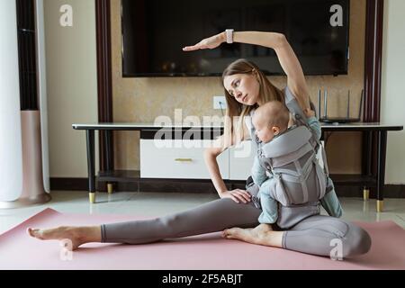 Junge Mutter in Sportkleidung Sport zu Hause mit Baby. Online-Schulung während der Coronavirus covid-19 Quarantäne. Bleiben Sie während einer Pandemie fit und sicher Stockfoto