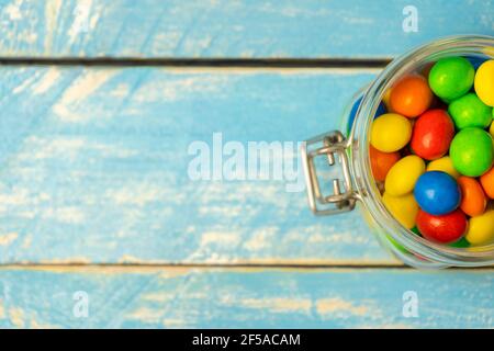 Bunte Schokolade Bonbons im Glas auf blauen vintage Holz Hintergrund.Draufsicht bunte Süßigkeiten Hintergrund Konzept mit Platz für Text kopieren. Stockfoto