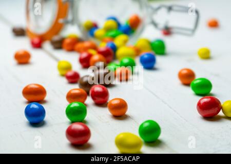 Nahaufnahme der verstreuten bunten Schokolade Bonbons auf weißem Holz Hintergrund.Multicolored Süßwaren und Süßigkeiten Hintergrundkonzept. Stockfoto