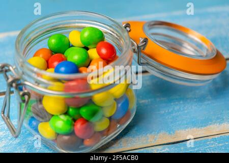 Bunte Schokoladenkugeln im Glas auf blauem Holzhintergrund.Bunte Süßigkeiten und Bonbons Hintergrund. Stockfoto