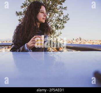 Junge Frau, die auf der Dachterrasse ein Bier trinkt Stockfoto