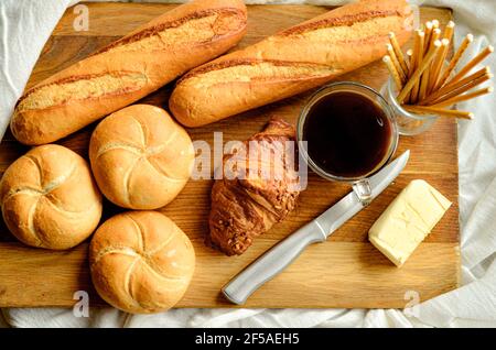 Frühstück auf einer weißen Tischdecke, Kaffee, Brötchen, Butter, Messer, Aus Holz Stockfoto