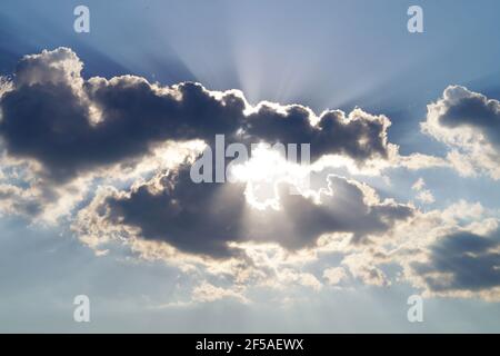 Die Sonnenstrahlen schauen hinter den grauen Wolken hervor Am Himmel Stockfoto