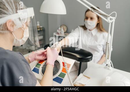 Junge Frau bekommen Maniküre im Schönheitssalon. Maniküre entfernen alte Maniküre. Frauen in Schutzmasken, Pandemie. Stockfoto