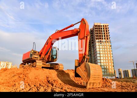 Bagger während der Aushubarbeiten auf der Baustelle auf Sonnenuntergang Hintergrund. Red Backhoe auf der Straße arbeiten. Schwere Baumaschinen für Erdarbeiten. Digger D Stockfoto