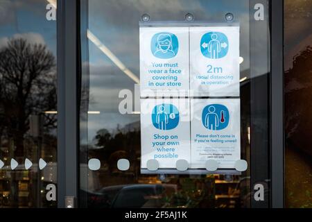 Ein Schild auf dem Fenster eines britischen Supermarkts, der berät Kunden der COVID 19- oder Coronavirus-Regeln für Käufer Betreten des Stores Stockfoto