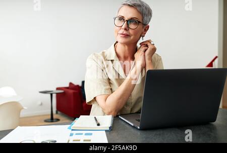 Nachdenkliche reife Frau mit Brillen an einem Schreibtisch sitzen Zu Hause Stockfoto