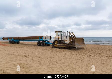 CAT Caterpillar D7H Series II Transport von großen Rohren auf Anhänger entlang Strand für Strand Nachschub Arbeit in Bournemouth und Poole Beaches, Dorset UK Stockfoto