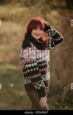 Vertikale Aufnahme einer lächelnden kaukasischen Frau mit roten Haaren Mit kuscheligem Pullover Stockfoto