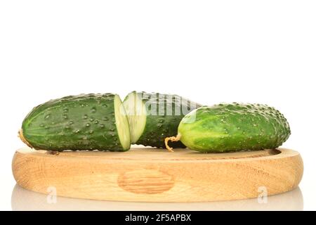 Eine ganze und zwei Hälften sind dunkelgrün, reif, organisch, frische Gurken, Nahaufnahme, Auf einem runden Tablett aus Bambus ist der Hintergrund weiß. Stockfoto