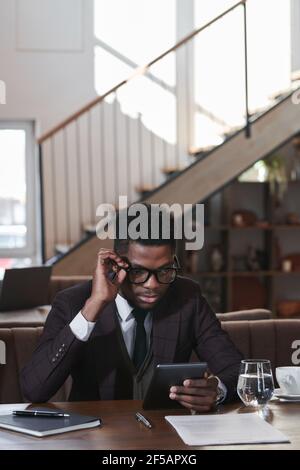 Afrikanischer Geschäftsmann, der beim Sitzen etwas auf einem digitalen Tablet sieht Der Tisch während des Mittagessens im Restaurant Stockfoto
