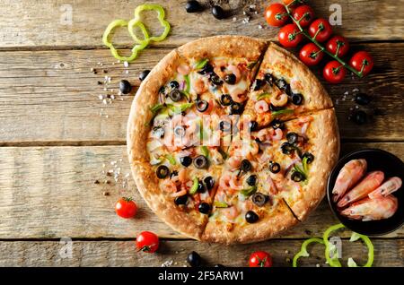 Pizza mit Garnelen, Oliven, grünem Pfeffer und Zwiebeln auf einem Holzhintergrund. Stockfoto