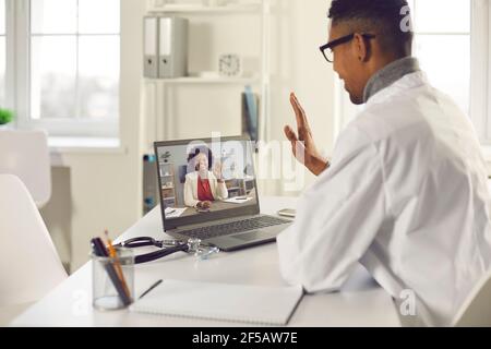 African american männlich Arzt Blick auf Laptop-Bildschirm winkende Hand Rückansicht Stockfoto
