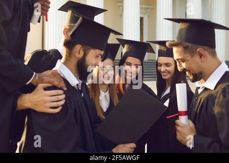 Gruppe von glücklichen Studenten in Mörtel Boards und Bachelor Mantel überprüfen die Graduation Album. Stockfoto