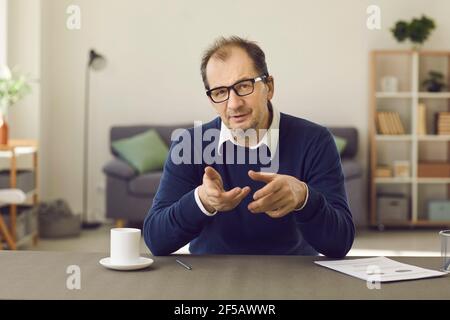 Ein männlicher Psychotherapeut mittleren Alters führt die Probleme des Patienten auf, indem er mit ihm über Video-Link spricht. Stockfoto