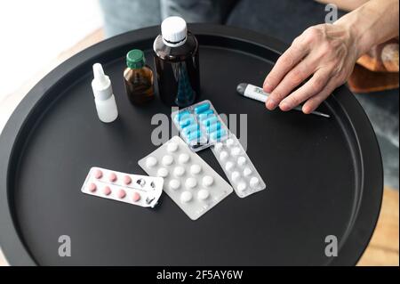 Draufsicht Tabletten, Pillen und verschiedene Behandlungsmittel auf dem Tisch in der Nähe der Couch nimmt eine weibliche Hand ein Thermometer. Gesundheitswesen und Medizin Konzept Stockfoto