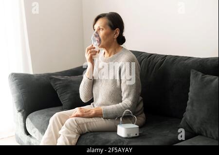 Frau im Rentenalter mit Inhalator für Grippe und Kälte Behandlung sitzen auf dem Sofa zu Hause, ältere Frauen decken Gesicht mit einer Sauerstoffmaske. Gesundheitswesen und Medizin Konzept Stockfoto