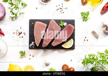 Frische rohe Thunfisch-Steaks auf schwarzem Schieferteller auf weißem Hintergrund. Draufsicht. Stockfoto