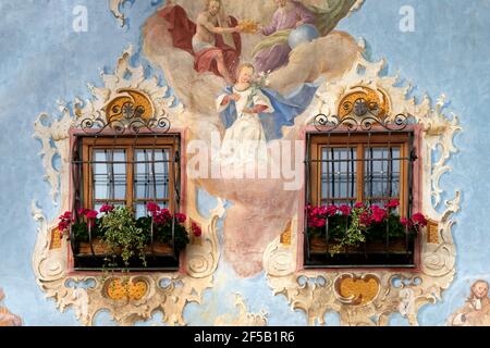 Nahaufnahme einer bemalten Fassade mit zwei Holzfenstern Und Geranien auf der Fensterbank Stockfoto