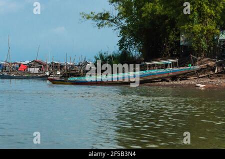 Traditionelles hölzernes Fischerboot in Asien, teilweise auf trockenem Land, im Hintergrund ein Fischerdorf Stockfoto