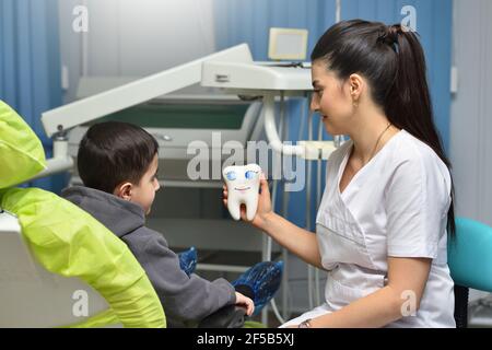 Frau Zahnarzt beruhigt ein Kind vor der zahnärztlichen Behandlung und Zeigt ihm einen großen Zahn Stockfoto