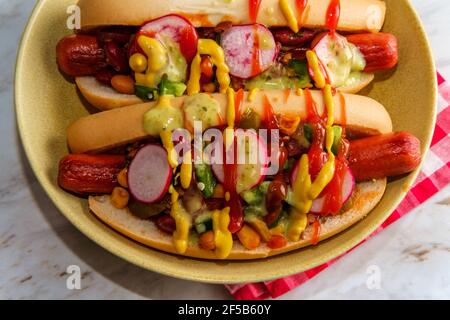 Ausgefallene Chili-Hunde mit Radieschen Senf Ketchup und grün gekrönt Soße auf glutenfreien Brötchen Stockfoto