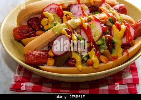 Ausgefallene Chili-Hunde mit Radieschen Senf Ketchup und grün gekrönt Soße auf glutenfreien Brötchen Stockfoto