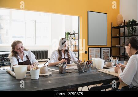 Töpferinnen während des Arbeitsprozesses in der Tonwerkstatt. Frau Meister bereiten Keramik-und Tonprodukte an großen Holztisch. Stockfoto