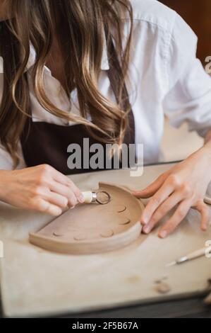 Frau, die mit Ton arbeitet, mit ihren Händen und einem Schleifenknirschwerkzeug, in einer Töpferwerkstatt Stockfoto