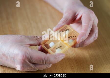 Nahaufnahme der Hände einer älteren älteren älteren Frau, die ihre Medikamente für die Woche in einer Pillenbox auf einem Holztisch einnahm, Geschäfts-, Gesundheits-Konzept Stockfoto