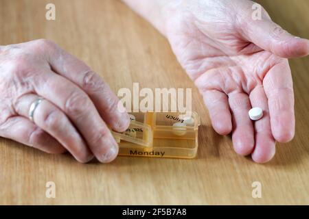 Nahaufnahme der Hände einer älteren älteren älteren Frau, die ihre Medikamente für die Woche in einer Pillenbox auf einem Holztisch einnahm, Geschäfts-, Gesundheits-Konzept Stockfoto