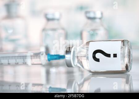 Impfstoffflasche mit hypodermischer Spritzennadel innen, Fragezeichen auf Etikett, Hintergrund der verschwommenen Fläschchen Stockfoto