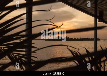 Abendstimmung auf dem Mekong. Blick durch ein Palmblatt auf die untergehende Sonne. Über die Uferfläche. Stockfoto