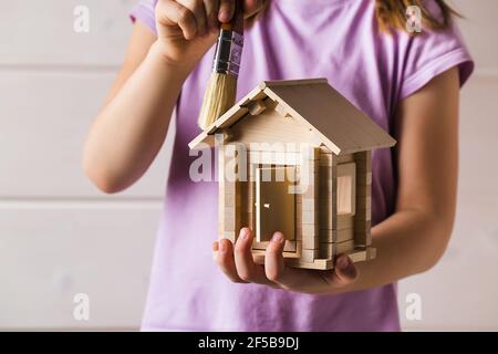 Kinder Hände mit Spielzeug Holzhaus und Pinsel, Home Services Konzept Stockfoto