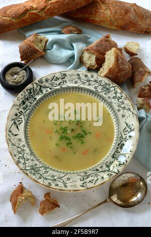 Gemüsesuppe mit Schnittlauch im antiken viktorianischen Stil Suppenschüssel mit vintage Suppenlöffel und zerrissene Stücke Frisch gebackene Baguettes Stockfoto